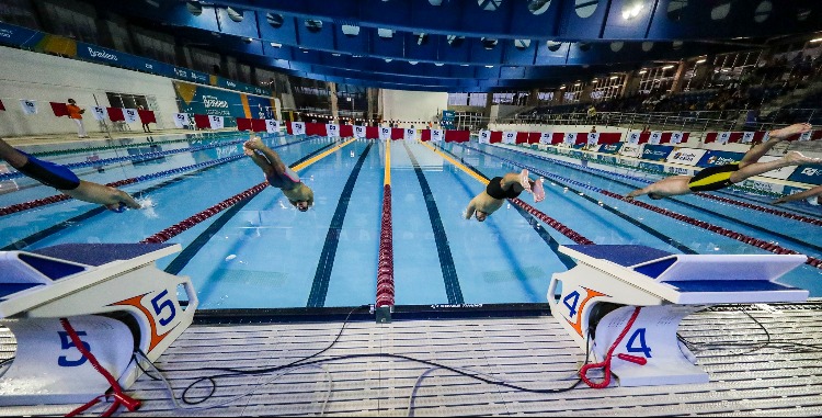 Atletas saltando do bloco de partida da natação na piscina do CT Paralímpico.
