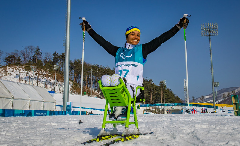 atleta negra sentada em um ski adaptado comemora vitória em pista de neve