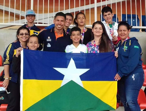 Equipe de paradesporto de Rondônia, com quatro professores e seis crianças, seguram a bandeira do estado de Rondônia e posam para foto nas arquibancadas do CT Paralímpico, em São Paulo