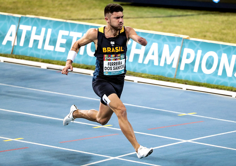 atleta com braço esquerdo amputado cruza a linha de chegada em pista de cor azul de atletismo