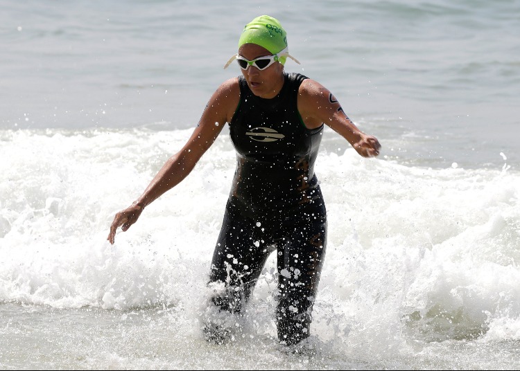 Atleta Ana Raquel Lins veste traje de neoprane preto, touca de natação amarela e óculos branco com preto. A atleta sai do mar no Rio de Janeiro durante os Jogos Rio 2016;