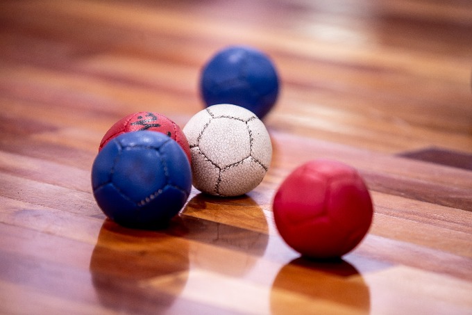 Quatro bolas de bocha estão sobre o chão liso. No centro está a bola branca e envolta dela duas bolas azuis e uma vermelha.