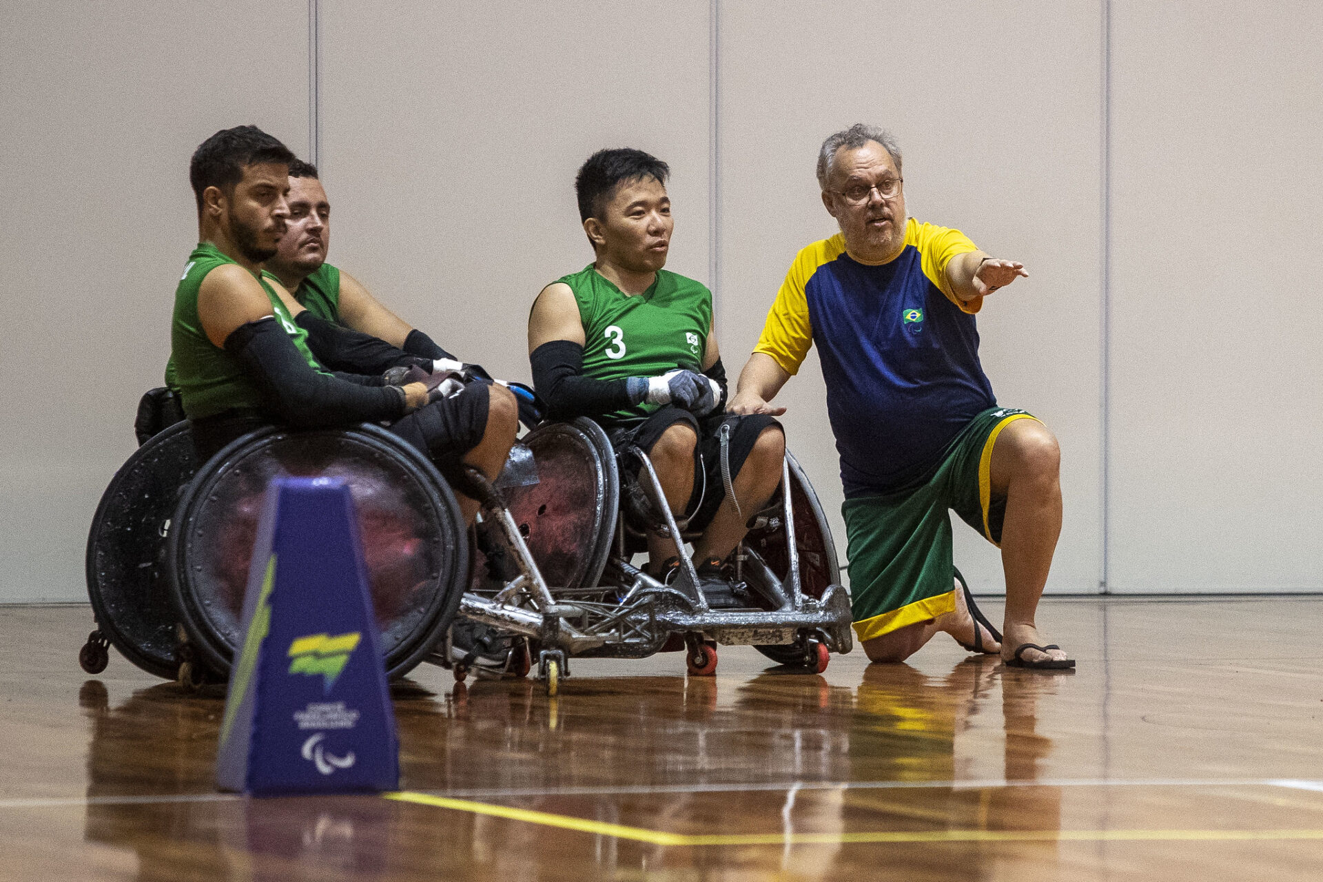 Treinador orienta jogadores de rúgbi em cadeira de rodas na quadra
